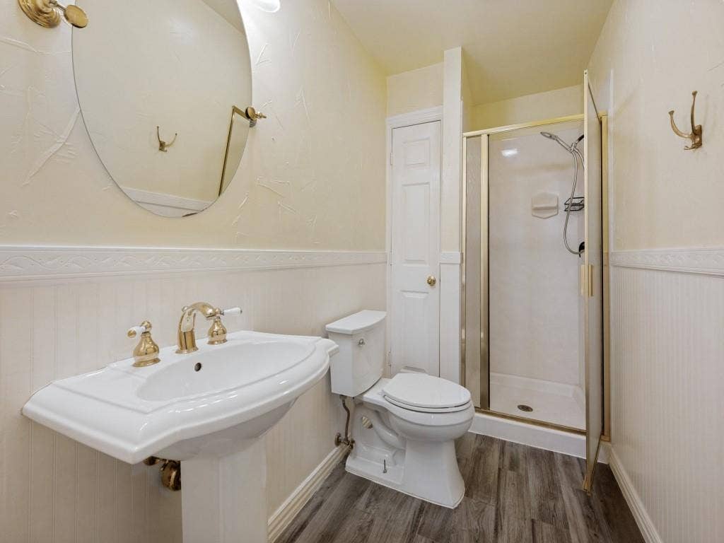9703 Raven Lane, Irving, TX 75063 Bathroom featuring a pedestal sink with brass-finish fixtures, a shower enclosure with a clear glass door, and wood-finish flooring