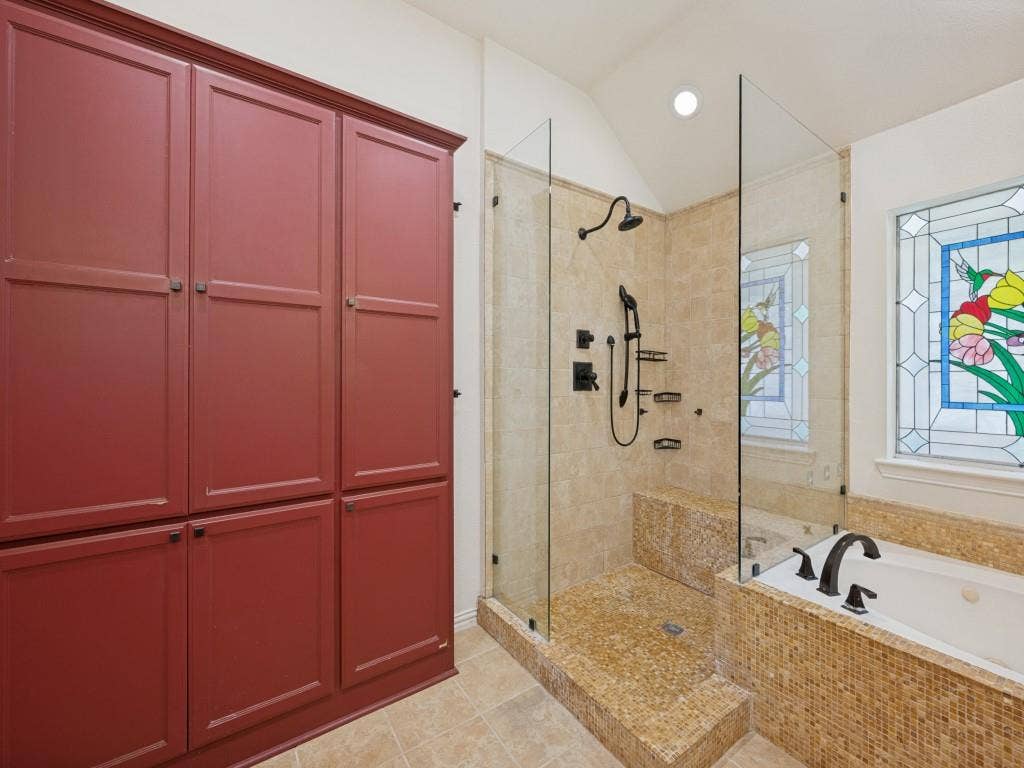 9703 Raven Lane, Irving, TX 75063 Built-in red cabinetry providing extensive storage, glass-enclosed shower with a built-in bench and multiple shower heads, jetted soaking tub, and decorative stained glass window