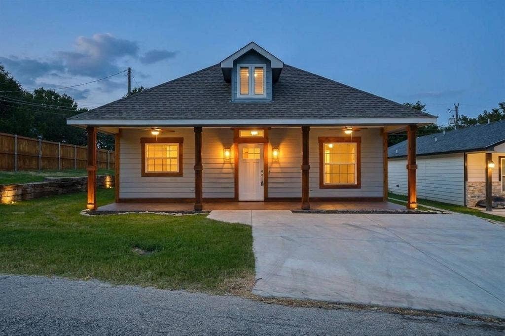 Exterior facade featuring horizontal siding, a covered front porch with timber posts, a gabled roofline with a dormer window, and a concrete driveway