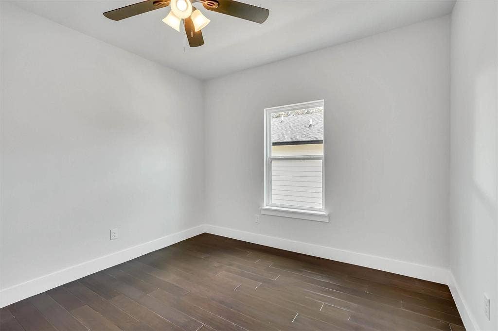 Contemporary room featuring wood-finish flooring, white baseboards, a ceiling fan with integrated lighting, and a double-hung window