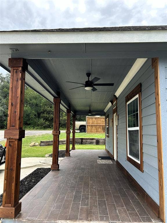 Expansive covered porch featuring tiled wood-like finish flooring, substantial cedar wood-clad support columns, and multiple ceiling fans
