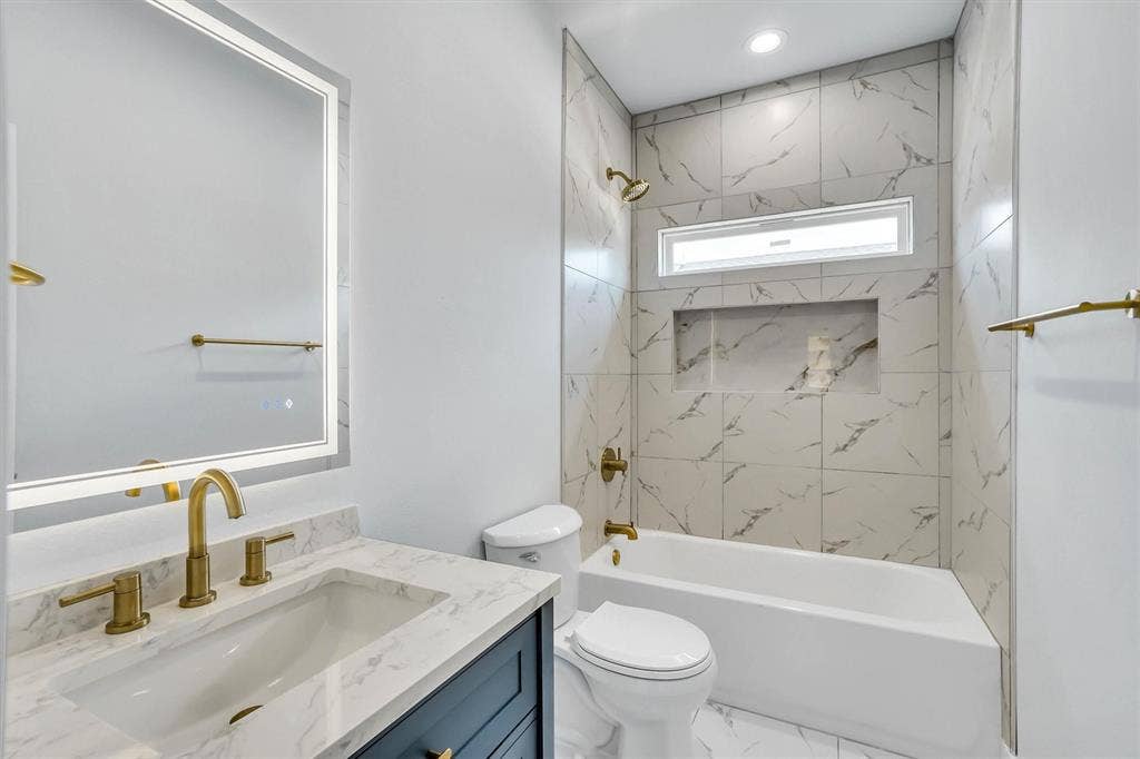 Bathroom featuring a white vanity with a marble-finish countertop, a single undermount sink, and brass-tone fixtures