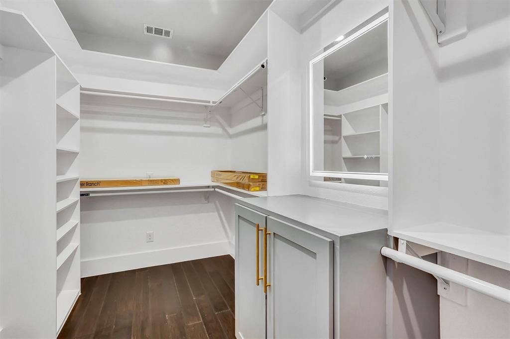 Custom closet system featuring dark wood-finish flooring, built-in shelving, hanging rods, and a central cabinet with gold-tone hardware