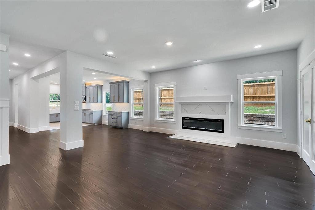 Spacious interior with dark wood-finish flooring, recessed lighting, and a modern fireplace featuring a white mantel and marble-patterned surround