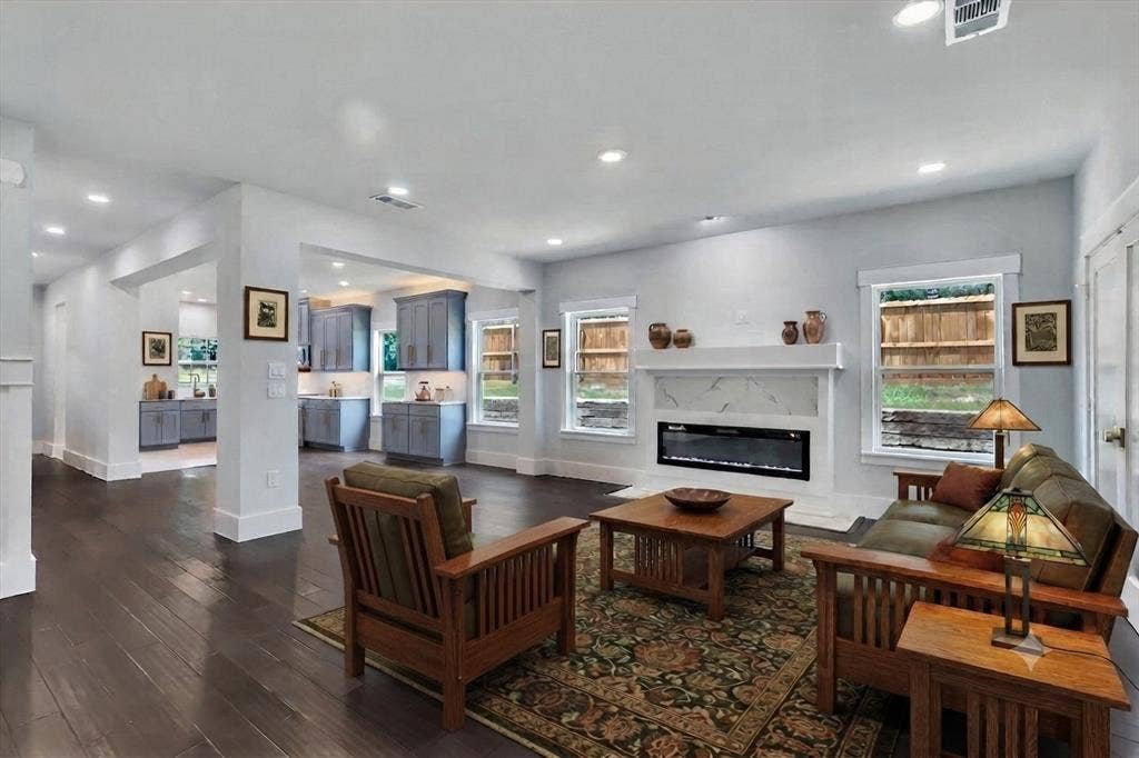 Spacious open-concept living area featuring dark wood-finish flooring, recessed lighting, and a modern fireplace with a white surround and mantel