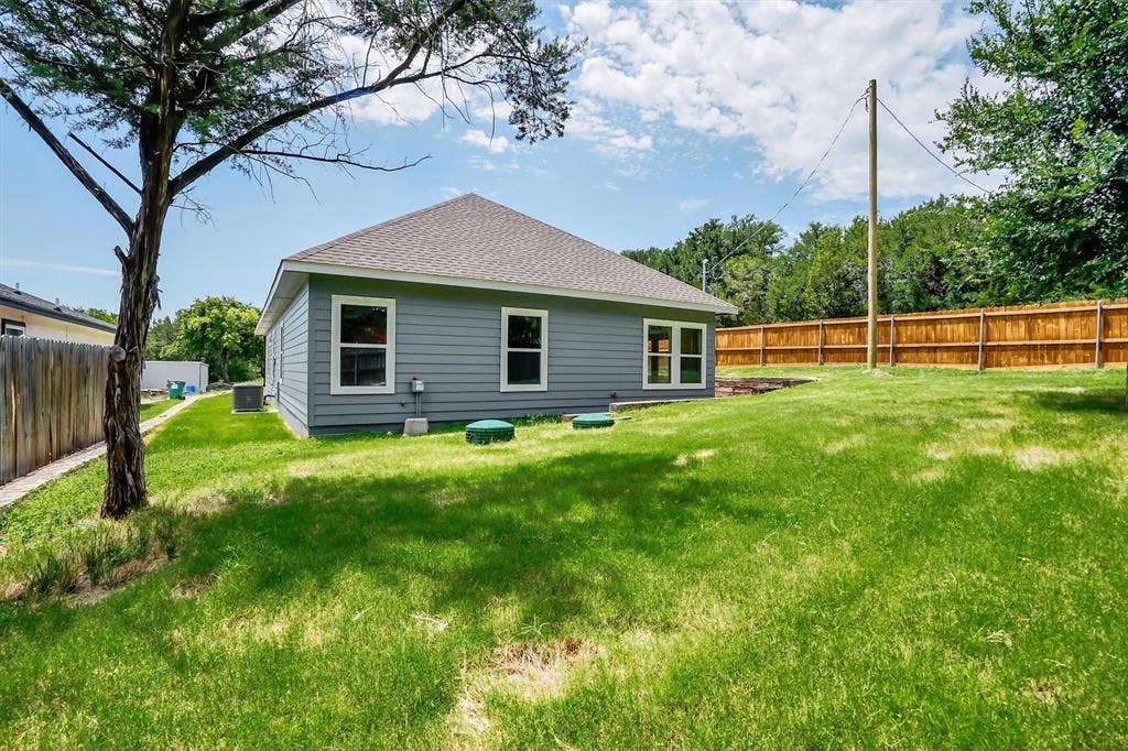 Expansive rear yard featuring green grass, a wood-paneled fence, and a gray-sided exterior with white-framed windows