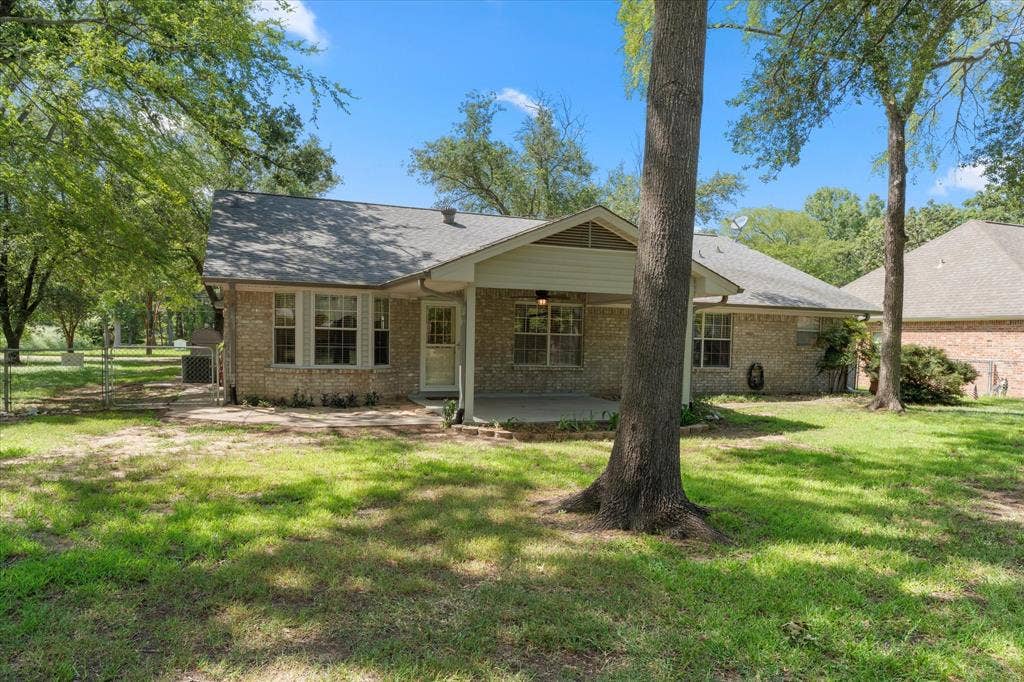 116 Meadowood Road, Enchanted Oaks, TX 75156 Brick exterior featuring multiple windows with louvered shutters, a covered patio, and a chain-link fence