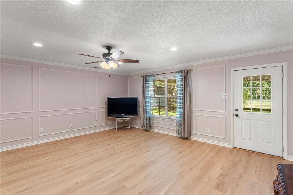 116 Meadowood Road, Enchanted Oaks, TX 75156 Spacious room featuring light wood-finish flooring, decorative wall molding, a ceiling fan with integrated lighting, recessed ceiling lights, and a white paneled door with a multi-pane glass insert