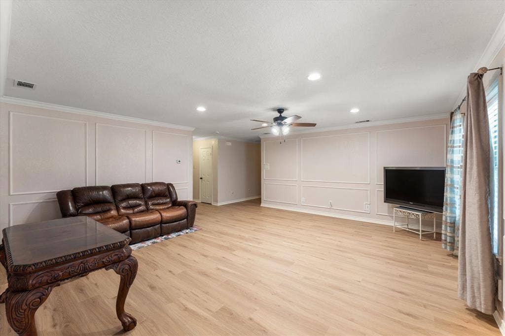 116 Meadowood Road, Enchanted Oaks, TX 75156 Spacious living area featuring light wood-finish flooring, decorative wall paneling, and a contemporary ceiling fan