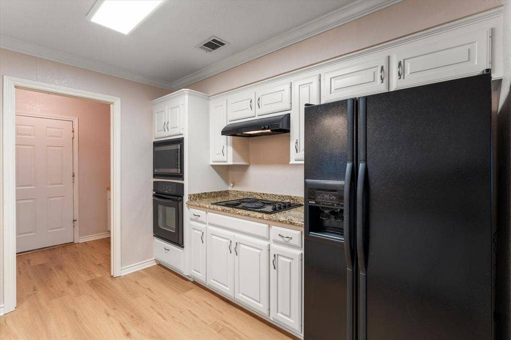 116 Meadowood Road, Enchanted Oaks, TX 75156 Kitchen featuring wood-finish flooring, white cabinetry with silver hardware, granite-style countertops, and black built-in appliances
