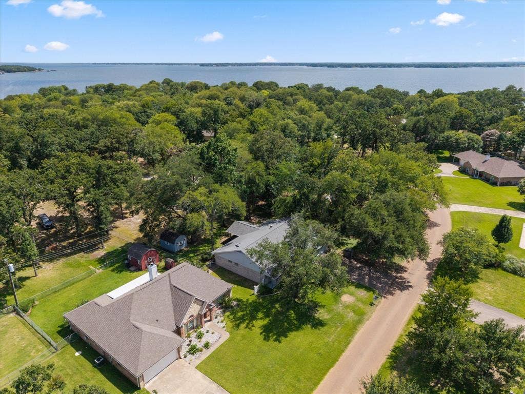 116 Meadowood Road, Enchanted Oaks, TX 75156 Aerial perspective showcasing a property surrounded by mature trees, with a large body of water visible in the distance