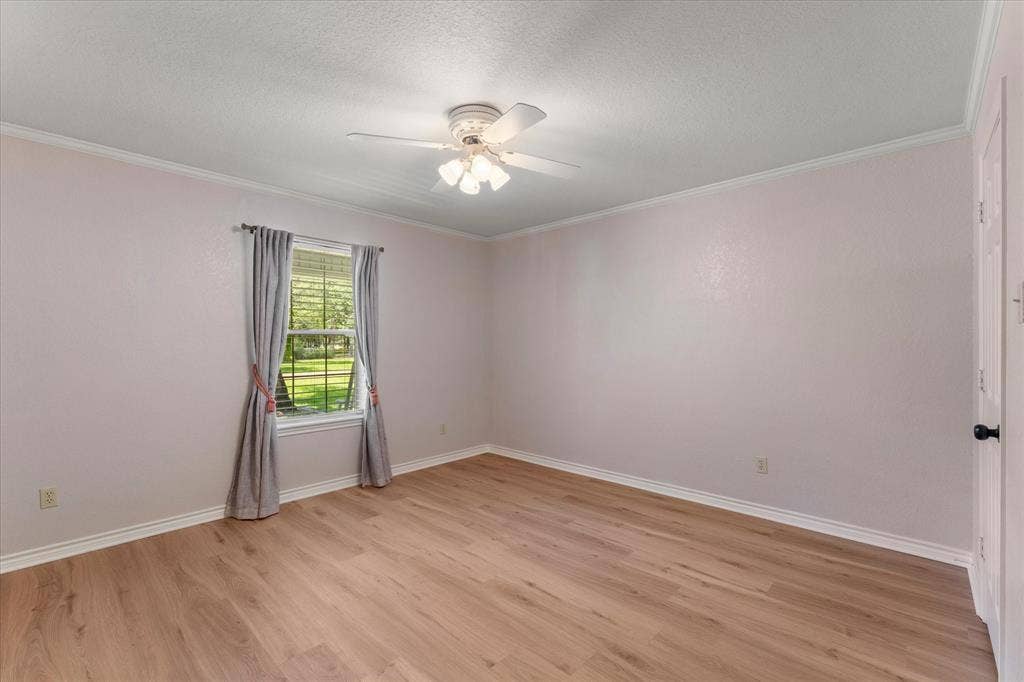 116 Meadowood Road, Enchanted Oaks, TX 75156 Spacious room featuring wood-finish flooring, a ceiling fan with integrated lighting, a window with exterior views, crown molding, and white baseboards