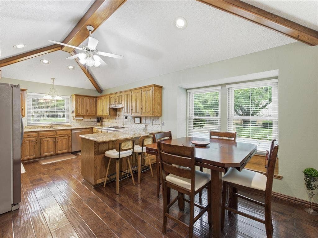 3701 Waycross Court, Arlington, TX 76016 Kitchen featuring wood-finish flooring, vaulted ceiling with exposed wood beams, wood cabinetry, light-toned countertops, and a window with horizontal blinds