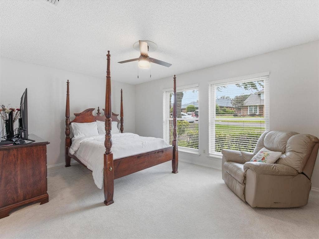 3701 Waycross Court, Arlington, TX 76016 Bright bedroom featuring light-colored carpet, white walls, two windows with blinds, and a ceiling fan with light fixture