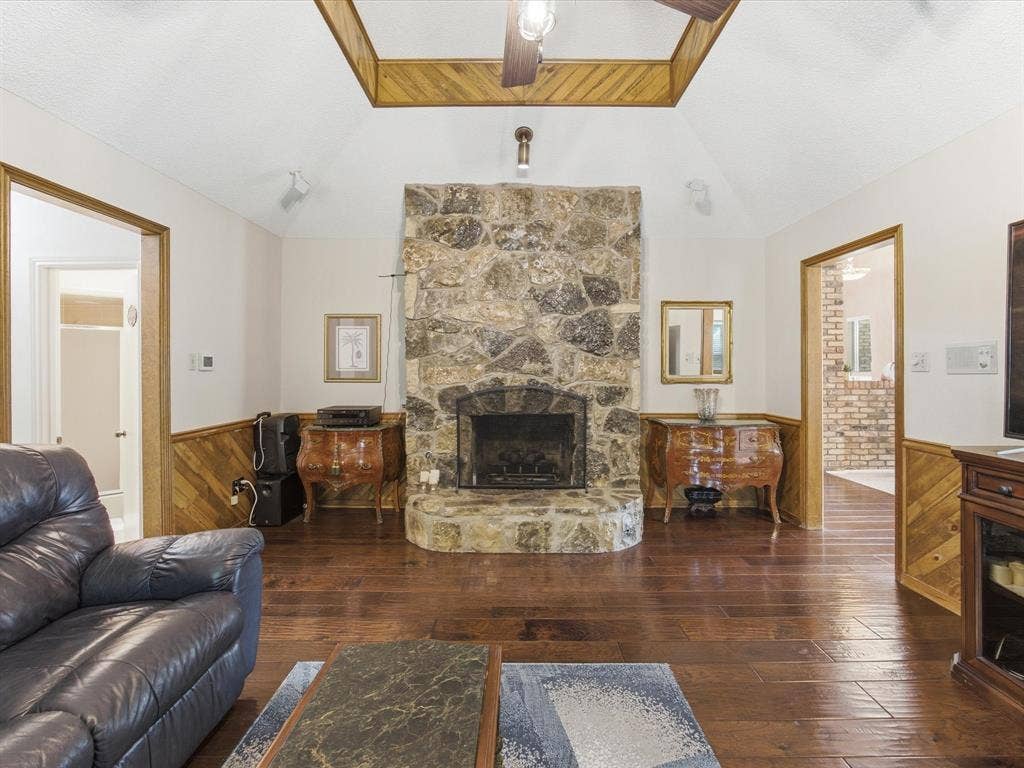 3701 Waycross Court, Arlington, TX 76016 Spacious living area featuring a stone fireplace with hearth, vaulted ceiling, wood-finish flooring, and wood paneling on lower walls