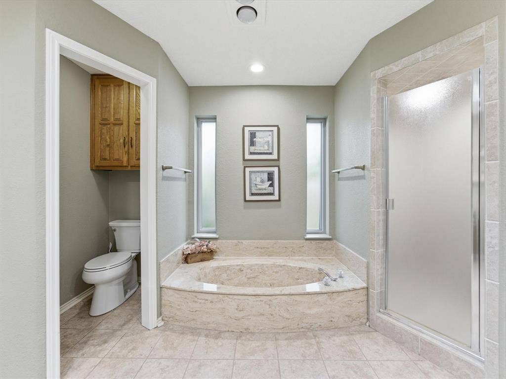3701 Waycross Court, Arlington, TX 76016 Primary Bathroom featuring a tiled soaking tub with marble-finish surround, a tiled walk-in shower with frosted glass enclosure, and light-colored tile flooring