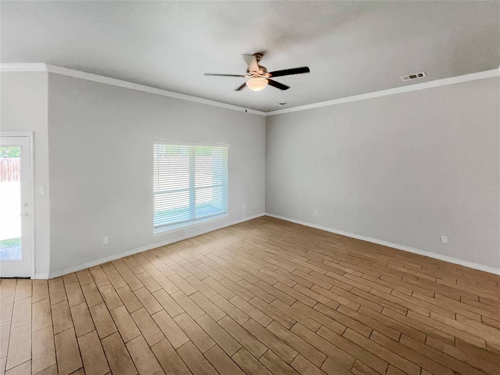 Spacious interior featuring wood-look tile flooring, crown molding, and a ceiling fan with integrated lighting