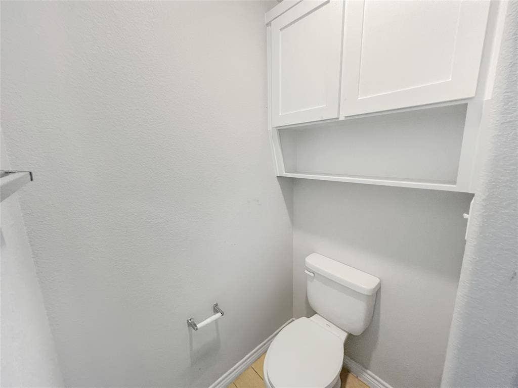 White toilet with built-in overhead cabinetry featuring two shaker-style doors and an open shelf