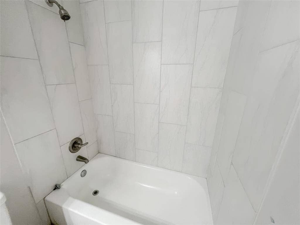 White bathtub with an integrated shower, surrounded by light-toned rectangular wall tiles
