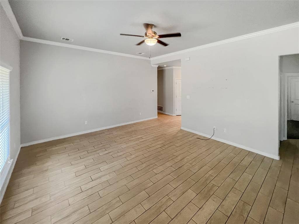 Spacious interior room featuring light-toned wood-finish tile flooring, neutral wall paint, and white crown molding