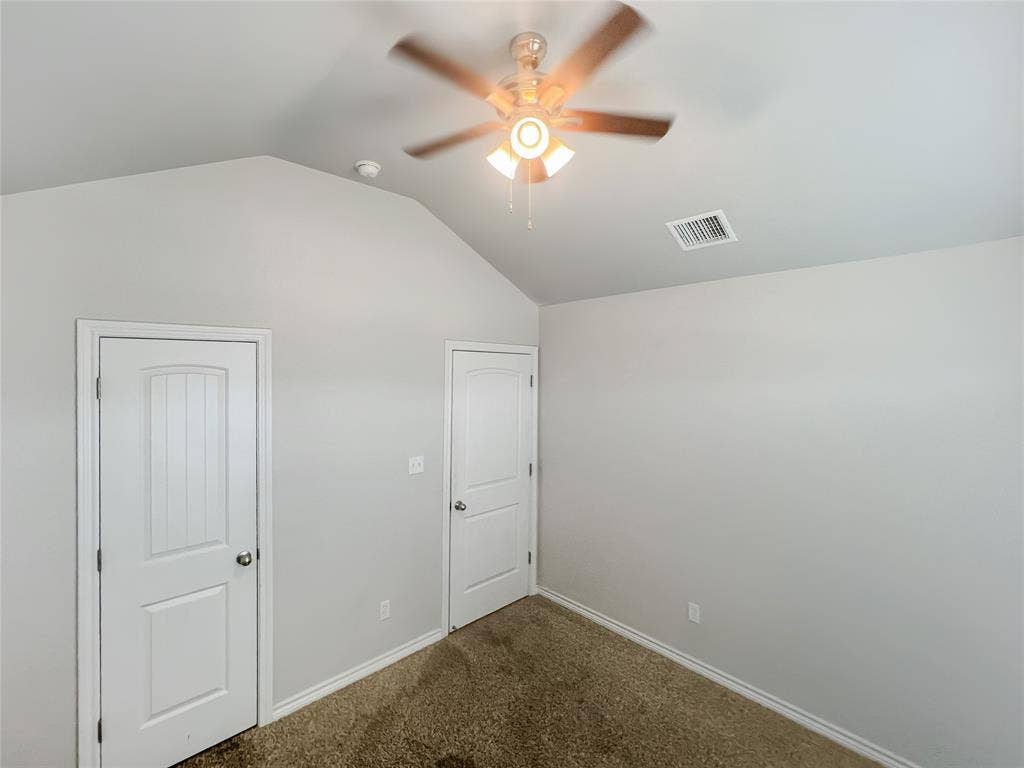 Vaulted ceiling with a ceiling fan light fixture, two panel doors, and neutral wall tones