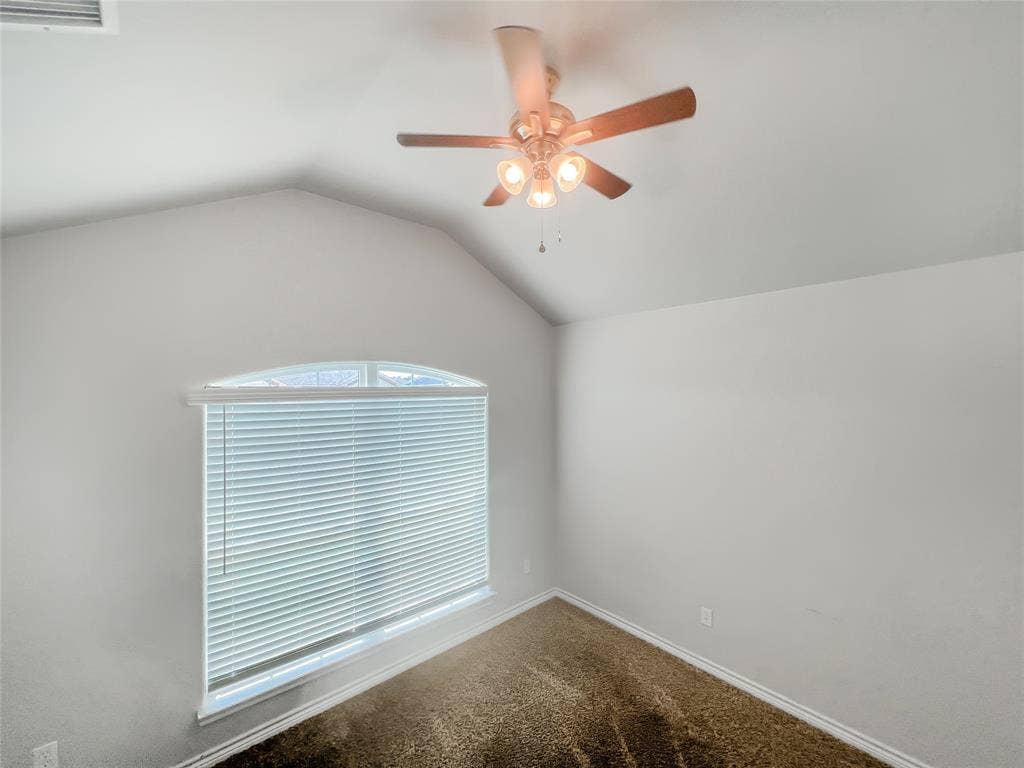 Room featuring vaulted ceilings, a ceiling fan with light fixture, window with arched transom, horizontal blinds, and carpet flooring