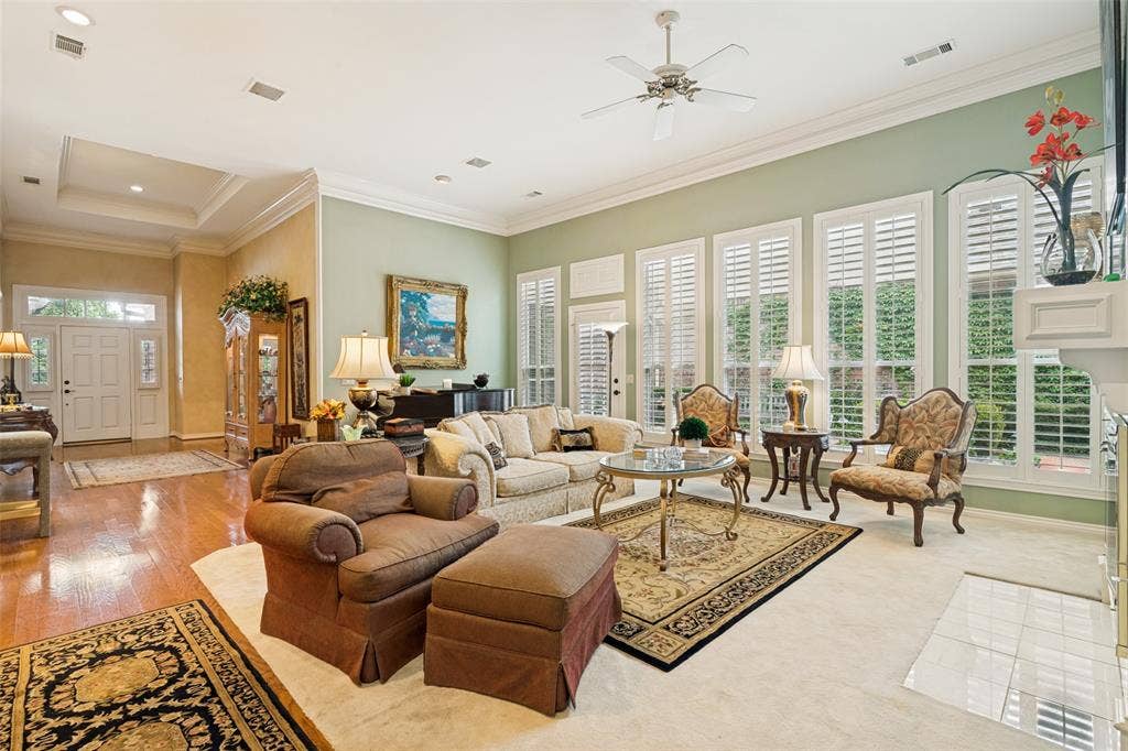 Spacious living area featuring high ceilings, crown molding, a ceiling fan, and multiple windows with plantation shutters