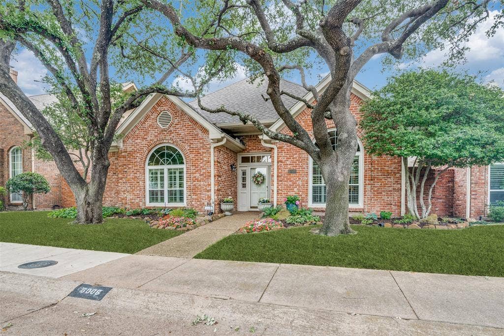 Red brick exterior featuring a white front door, arched windows, and mature trees framing the property