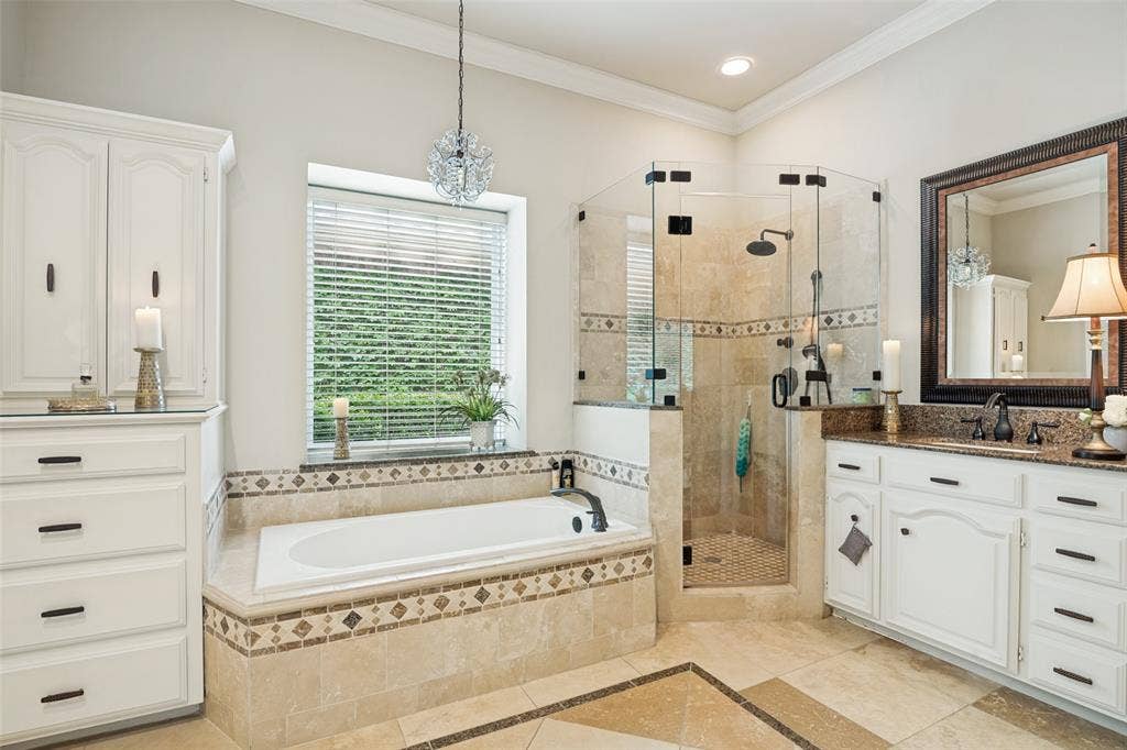 Expansive bathroom featuring a built-in soaking tub, a glass-enclosed shower, a double vanity with stone countertop, and custom white cabinetry