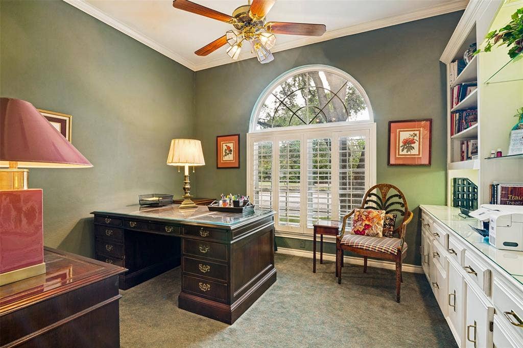 Room featuring a large arched window with plantation shutters, built-in shelving, white cabinetry with gold-tone hardware, and a ceiling fan