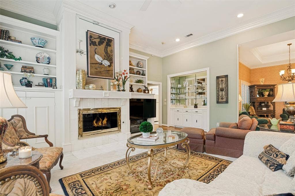 Living area featuring a fireplace with a white mantel, built-in shelving, recessed lighting, crown molding, and a built-in display cabinet
