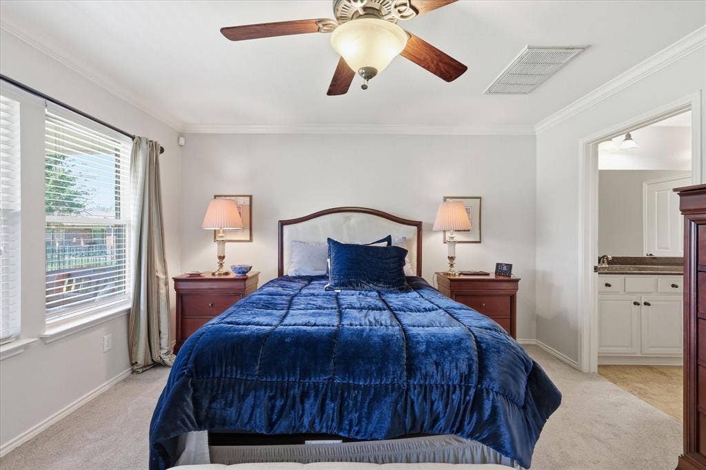 7594 Trull Brook Lane, Frisco, TX 75036 Carpeted bedroom featuring a ceiling fan with integrated lighting, crown molding, and dual windows with blinds and Ensuite Bathroom