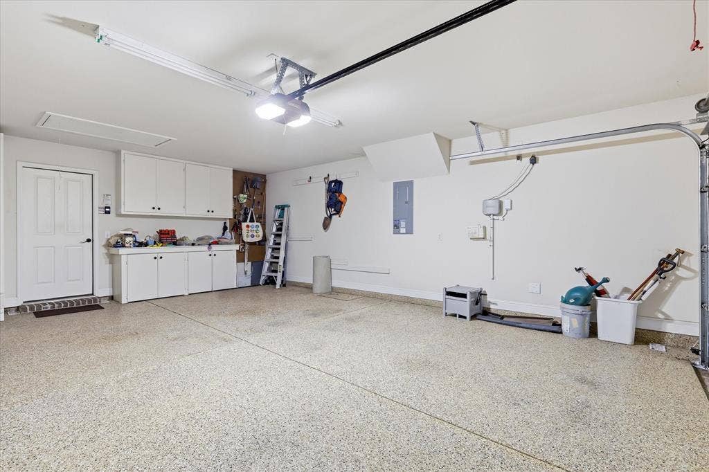 7594 Trull Brook Lane, Frisco, TX 75036 Spacious garage featuring a durable speckled epoxy floor, built-in white cabinetry, a dedicated workbench area, ample overhead lighting, and an automatic garage door opener
