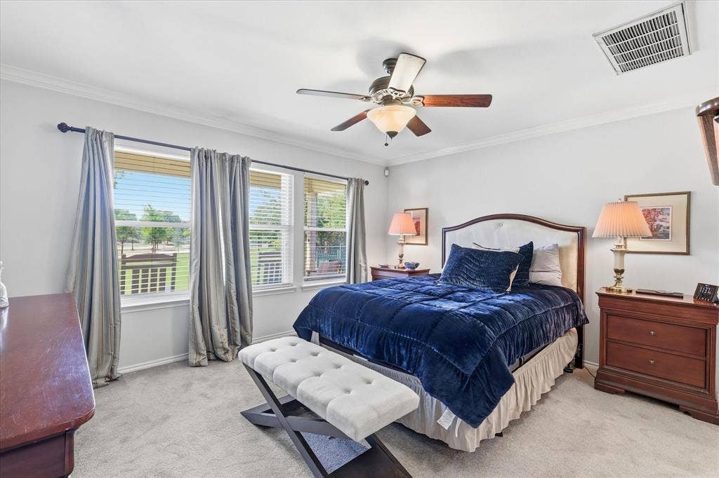 7594 Trull Brook Lane, Frisco, TX 75036 Bedroom featuring triple windows with blinds and curtains, a ceiling fan with integrated lighting, crown molding, and light-colored carpeting