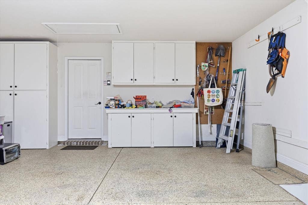 7594 Trull Brook Lane, Frisco, TX 75036 Garage interior featuring abundant white cabinetry, a built-in workbench, an epoxy-coated concrete floor, a service door, and attic access