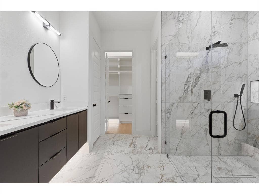 Contemporary bathroom featuring a spacious glass-enclosed shower with black fixtures and large format marble-look tile