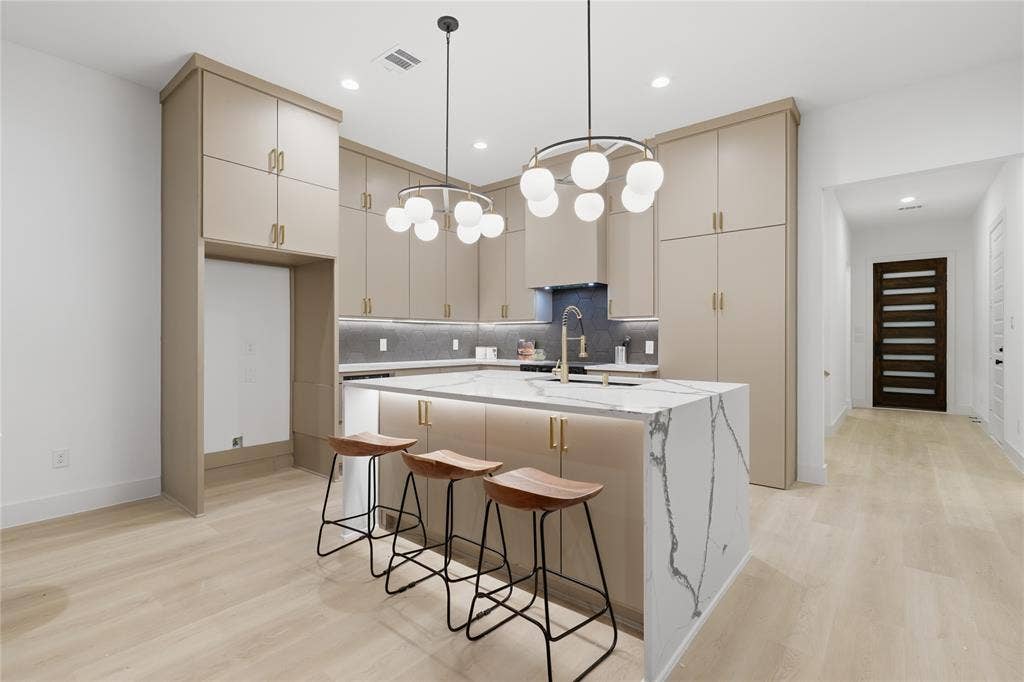 Modern kitchen featuring a waterfall island with a quartz countertop, sleek cabinetry with gold-tone hardware, and contemporary globe pendant lighting