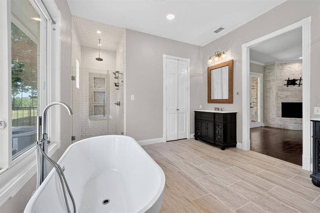 1201 Robbins Road, Athens, TX 75751 Experience luxury living in this beautifully designed primary bathroom, featuring a captivating view of a brick wood-burning fireplace from the primary bedroom. This exquisite space combines comfort and elegance, transforming everyday moments into a relaxing retreat.
