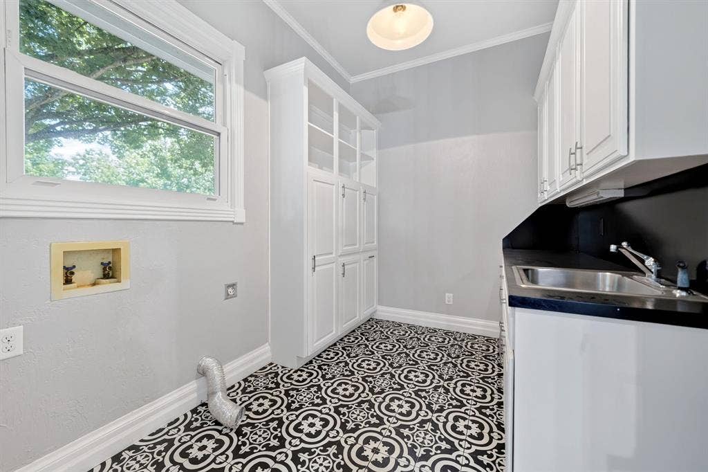 1201 Robbins Road, Athens, TX 75751 Laundry room featuring decorative black and white floor tiling, white built-in cabinetry, a utility sink. A window offers natural lighting and a view of the back yard area.