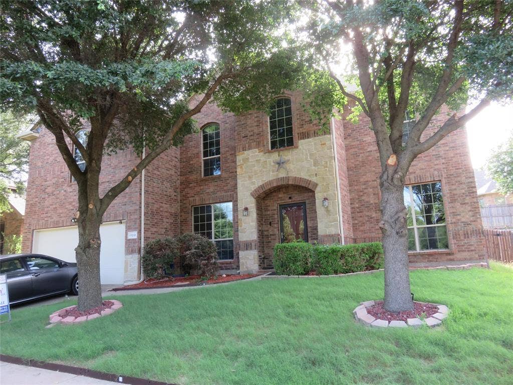 1122 Walter Stephenson Road, Midlothian, TX 76065 Brick and stone facade featuring an arched entryway, two prominent trees, a two-car garage, and established landscaping