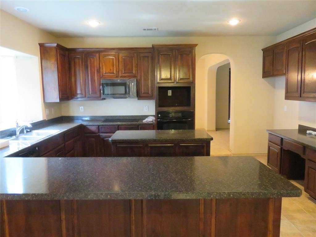 1122 Walter Stephenson Road, Midlothian, TX 76065 Kitchen featuring dark wood cabinetry, speckled countertops, a double basin sink, built-in microwave, and arched doorway