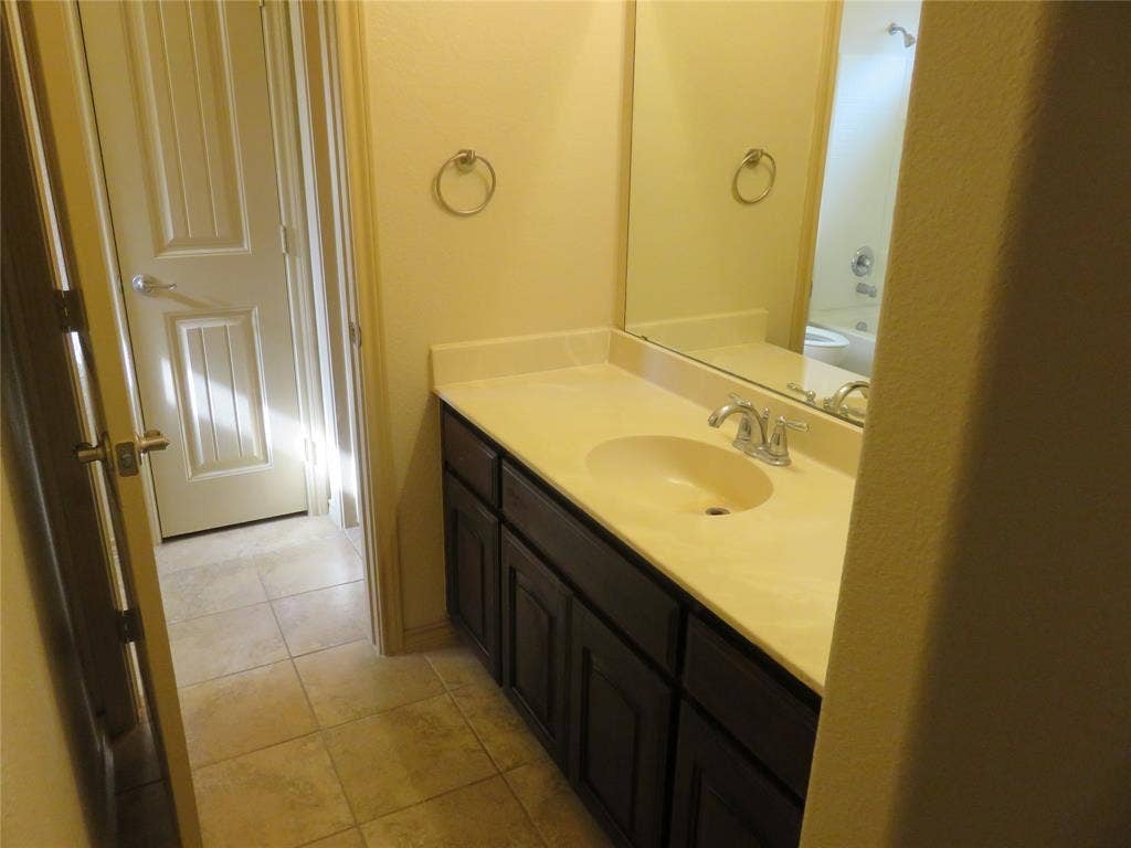 1122 Walter Stephenson Road, Midlothian, TX 76065 Bathroom vanity featuring a light-toned countertop with integrated sink, dark wood-finish cabinetry, and an expansive wall mirror