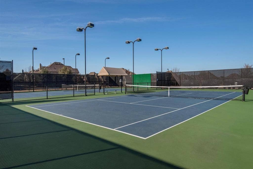 3861 Dalea Drive, Prosper, TX 75078 Blue-surfaced tennis court with white line markings, surrounded by a black chain-link fence