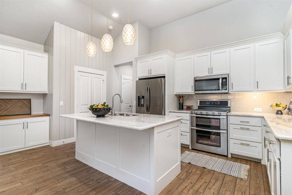 3861 Dalea Drive, Prosper, TX 75078 Kitchen featuring a central island with an undermount sink, white cabinetry, stainless steel appliances, marble-finish countertops, and wood-finish flooring