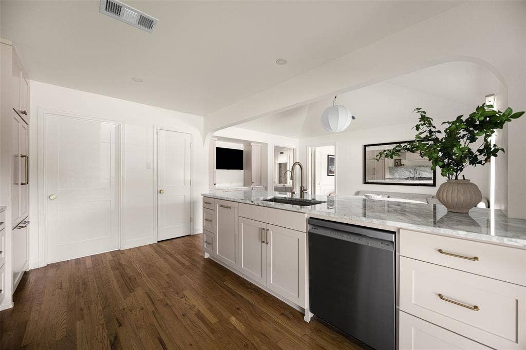 6501 Copper Creek Drive, Dallas, TX 75248 Kitchen island featuring a stainless steel sink with a gooseneck faucet, light-toned cabinetry, and a light-colored stone countertop