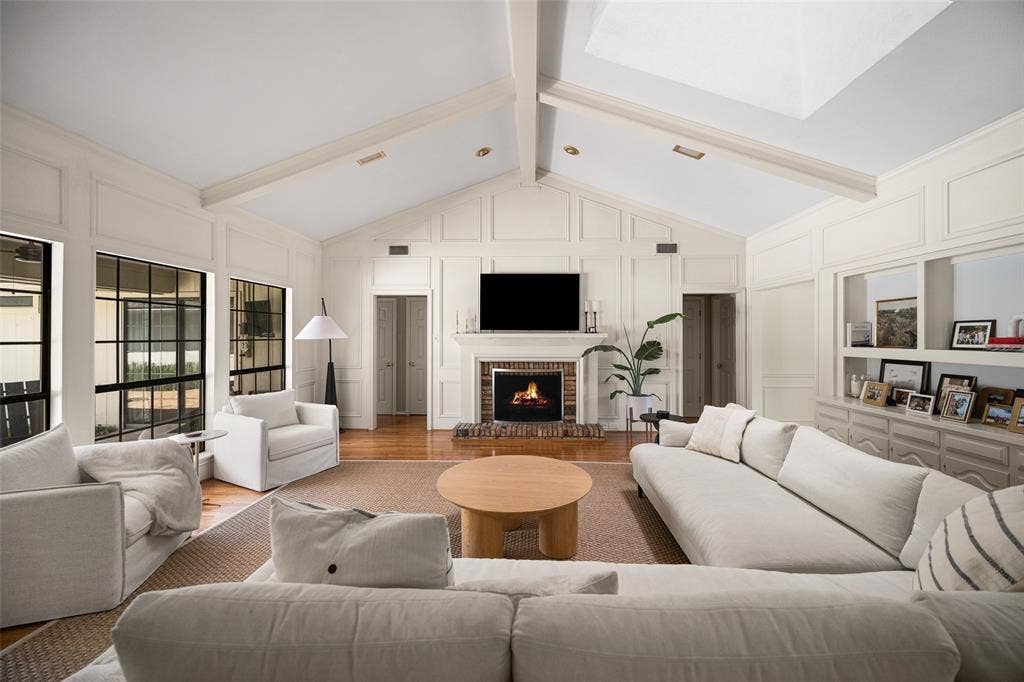 6501 Copper Creek Drive, Dallas, TX 75248 Living area featuring a brick fireplace with a mantle, vaulted ceilings with exposed beams, wood-finish flooring, and large grid-pattern windows