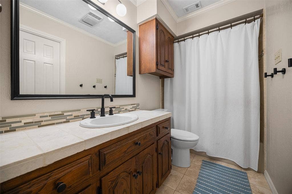 6501 Copper Creek Drive, Dallas, TX 75248 Bathroom vanity featuring a tiled countertop, undermount sink, matte black faucet, and a large framed mirror