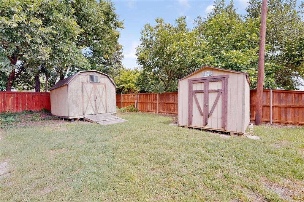 Expansive backyard featuring two utility sheds, a brown privacy fence, and mature trees