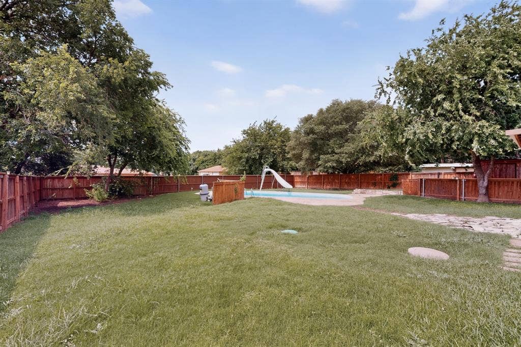 Spacious backyard featuring a rectangular swimming pool with a slide, surrounded by a wood privacy fence