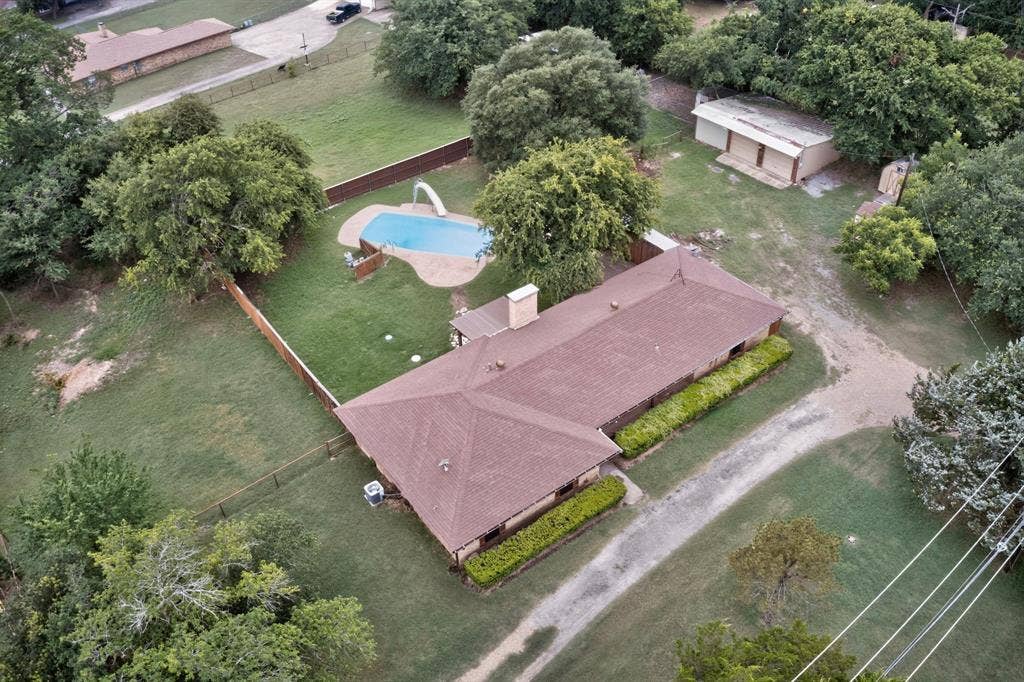 Expansive property featuring a single-story residence with a brown shingle roof, an inground swimming pool with a slide, a detached utility building, and mature perimeter trees